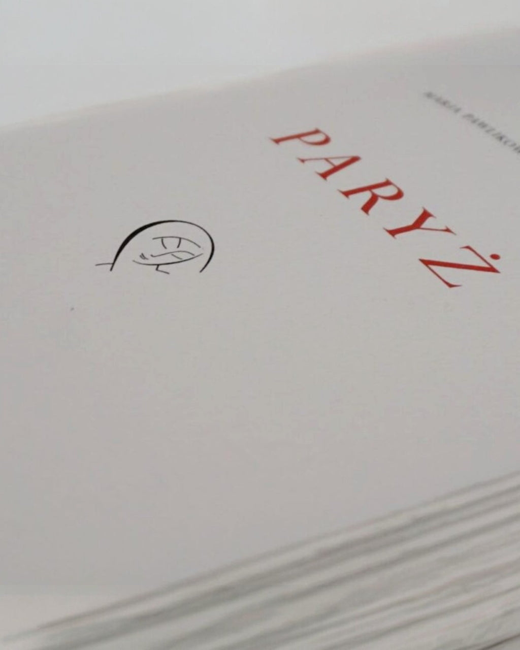 Zbliżenie strony tytułowej książki „Paryż” Marii Pawlikowskiej-Jasnorzewskiej z czerwonym napisem i minimalistyczną ilustracją na papierze bawełnianym.