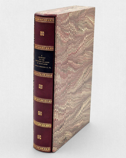 Bordowa, skórzana książka „A Journey to the Western Islands of Scotland” ze złoconymi zdobieniami na grzbiecie, wsunięta w ozdobne etui pokryte papierem marmurkowym w odcieniach brązu, beżu i czerwieni.