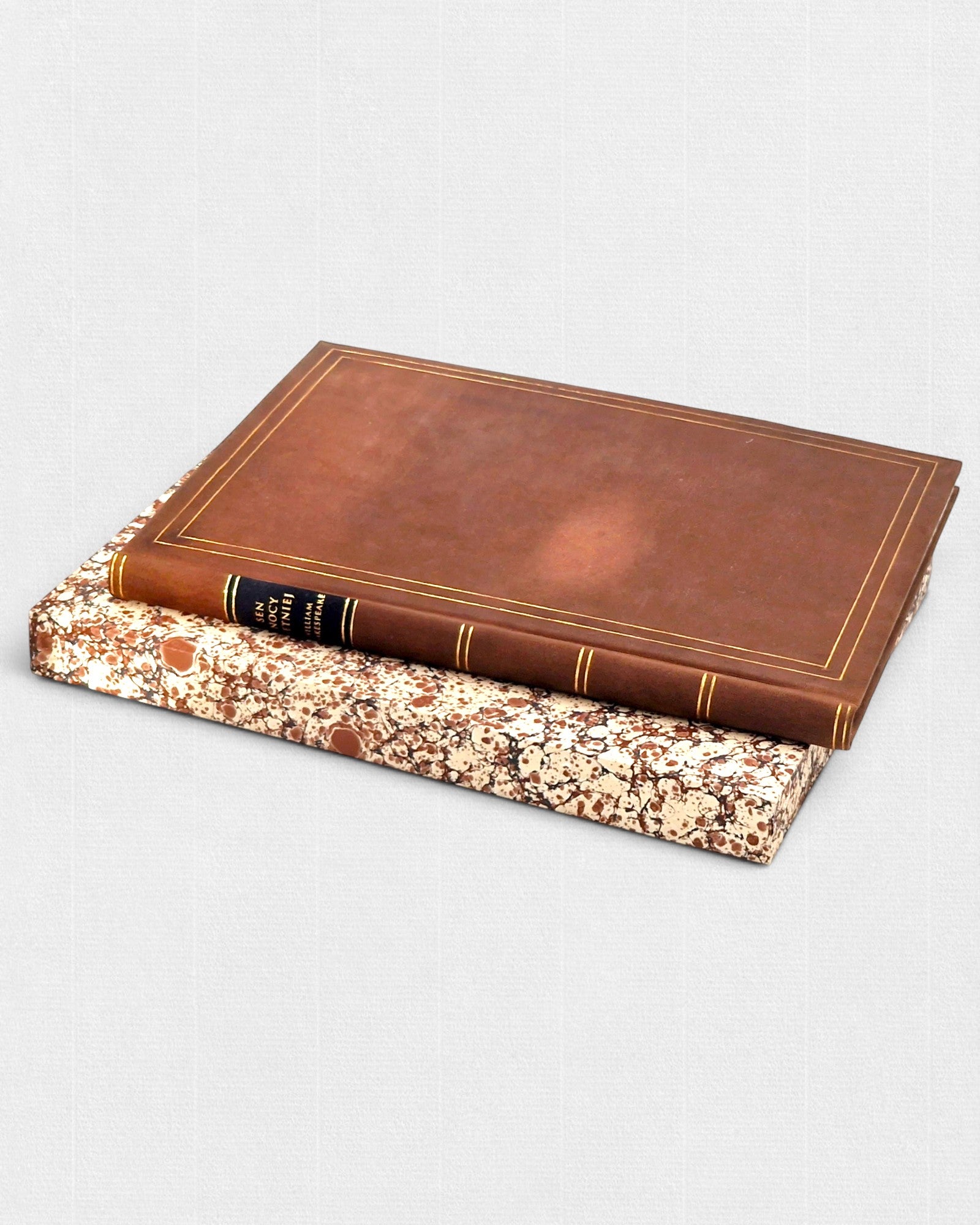 Ręcznie oprawiony egzemplarz Snu nocy letniej Williama Shakespeare’a w brązowej skórze ze złoconymi liniami, ułożony na etui pokrytym papierem marmurkowym.