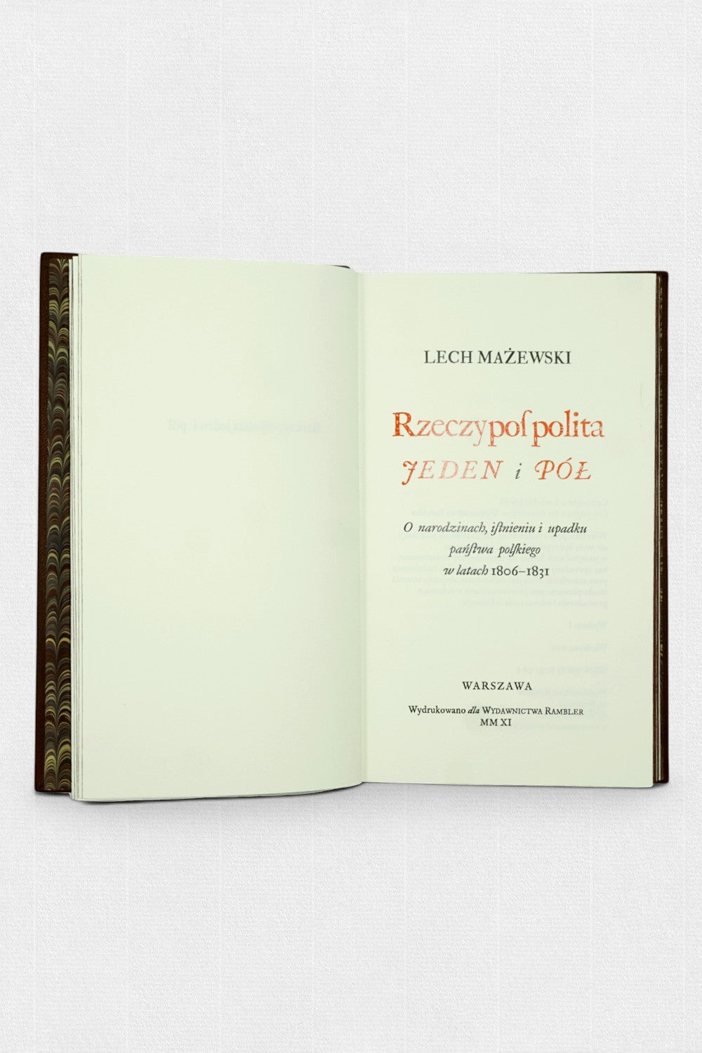 Otwarta książka z widoczną stroną tytułową „Rzeczpospolita jeden i pół” autorstwa Lecha Mażewskiego; po lewej marmurkowa wyklejka, po prawej karta tytułowa z czerwonym i czarnym drukiem.
